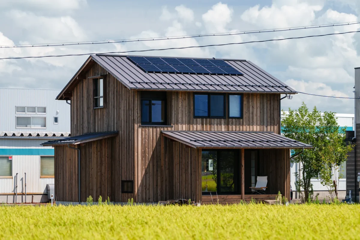 木板張りの外壁と金属屋根を持つ二階建て住宅、屋根上に太陽光パネルが設置されている