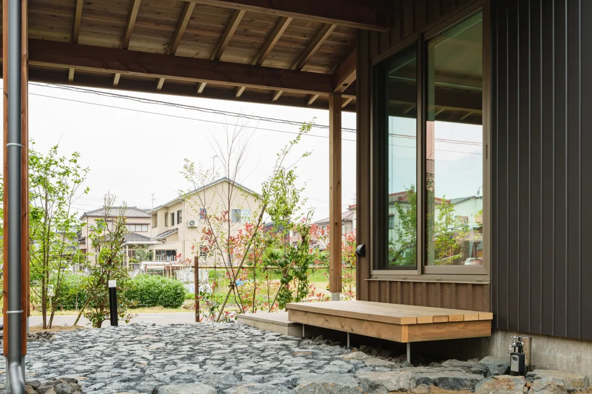 木製の庇と大きな窓がある住宅の庭側から見た外観。庭には石敷きが敷かれ、植栽が配置されている